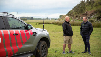 WK advisor speaking with a rural business owner beside a branded vehicle on farmland, discussing business strategy and financial advice.